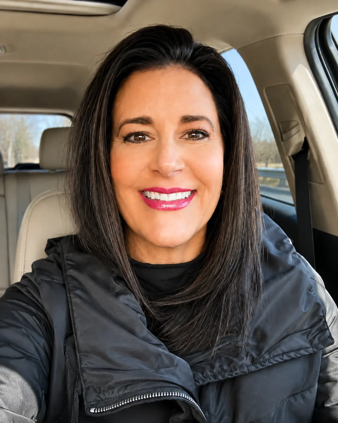 Diana Gentile smiling from the driver's seat of her car, sunlight coming through the windows